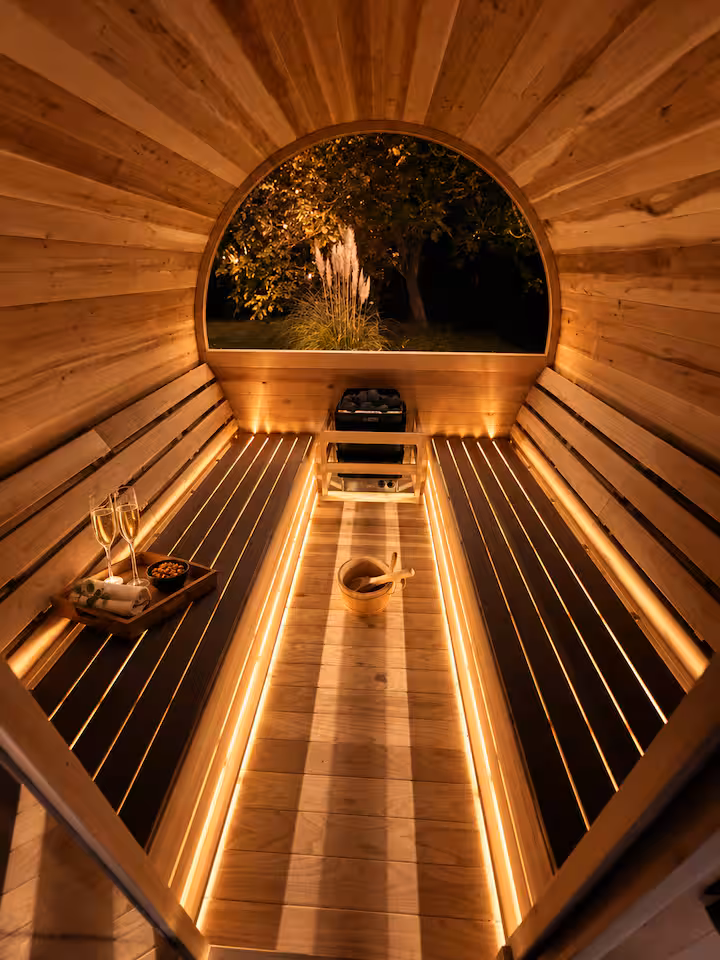 Inside the outdoor barrel sauna with warm lighting and a garden view